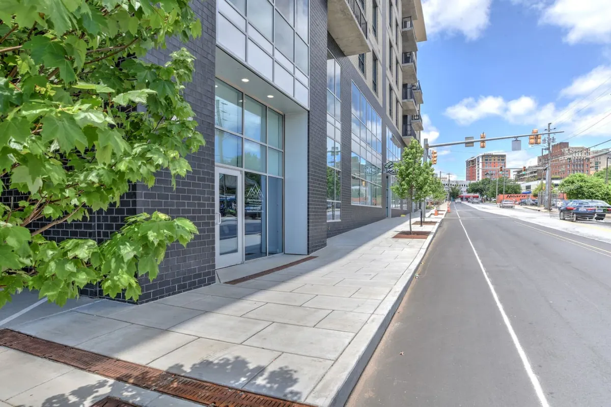 A lively street scene featuring the condo’s modern building facade, large glass windows, and a tree-lined sidewalk bustling with people. The image hints at the vibrant urban environment just steps outside, with easy access to shops, cafes, and cultural attractions.