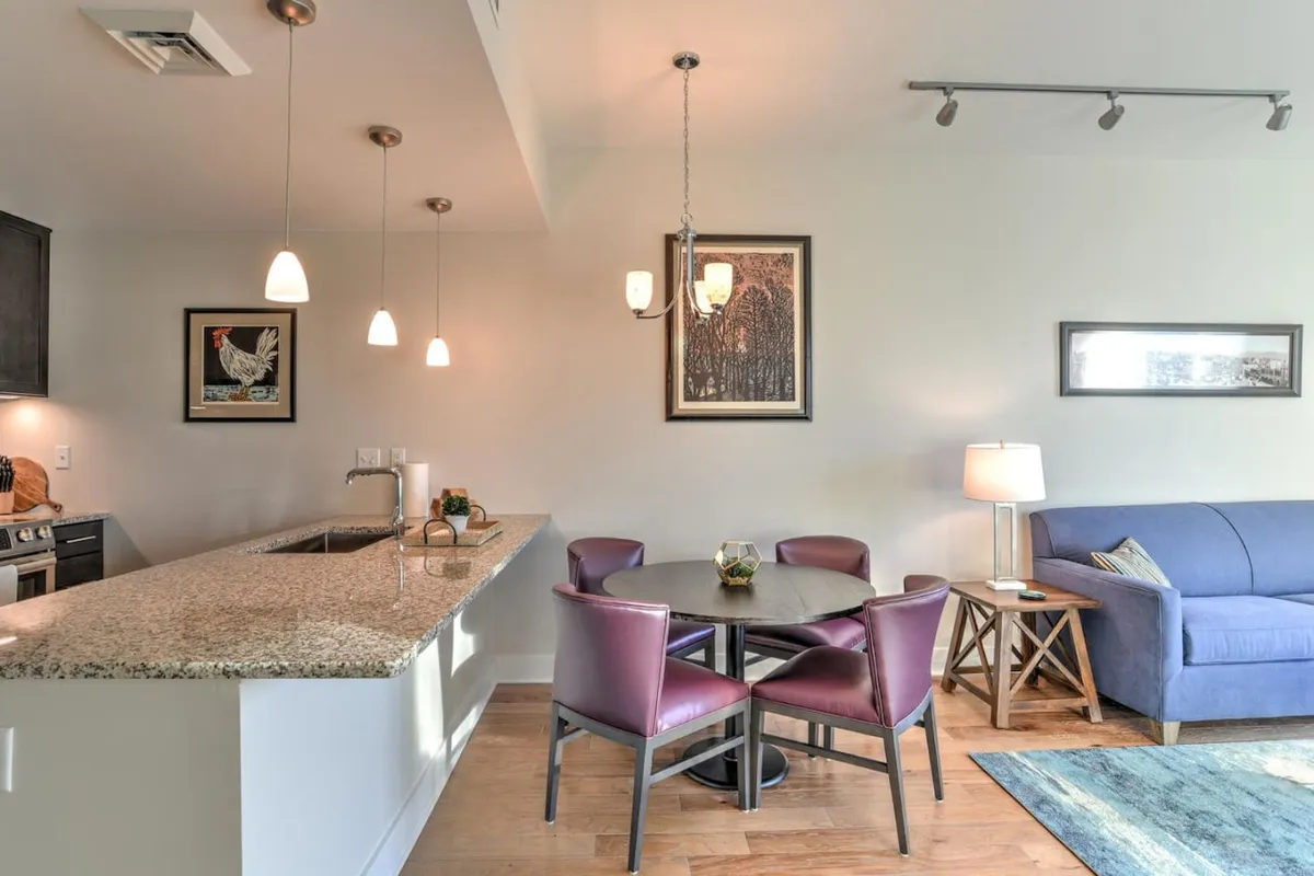 The scene captures a cozy interior with a granite countertop, dining table, sofa, and curated artwork on the walls. The setup is suited for activities ranging from dining and cooking to lounging and enjoying intimate conversations, showcasing an inviting and versatile open space.
