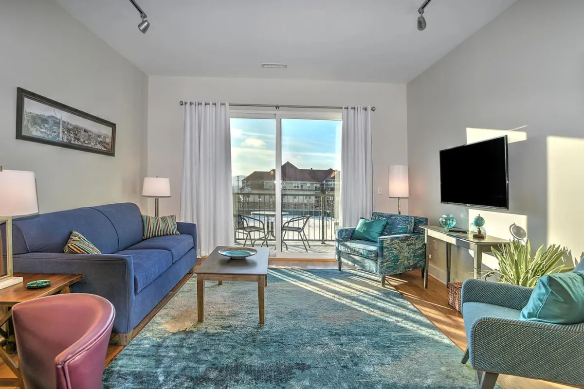 A cozy and welcoming interior living area featuring a comfortable sofa, armchair, and coffee table, with daylight streaming through a window that hints at city views. The space is arranged for relaxation and family togetherness after a day out.