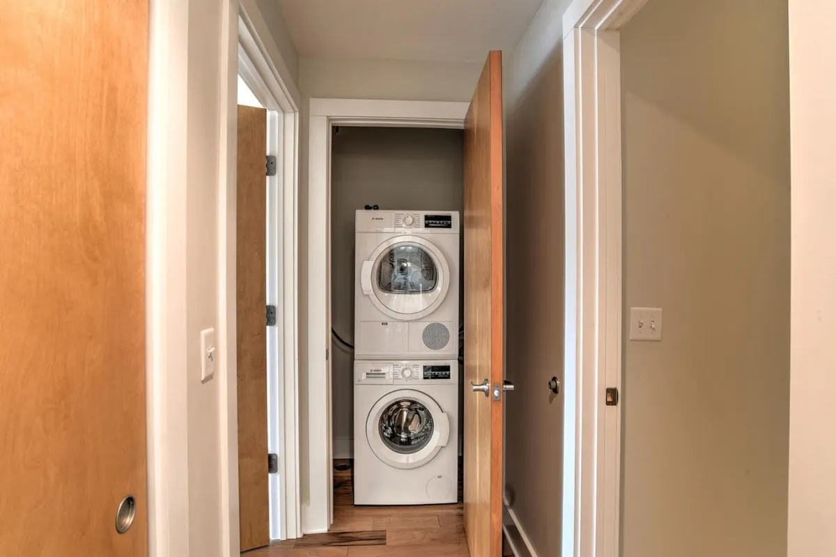 The image features a laundry area with a washer, dryer, and wooden doors against light-colored walls, presenting a functional and well-maintained space.