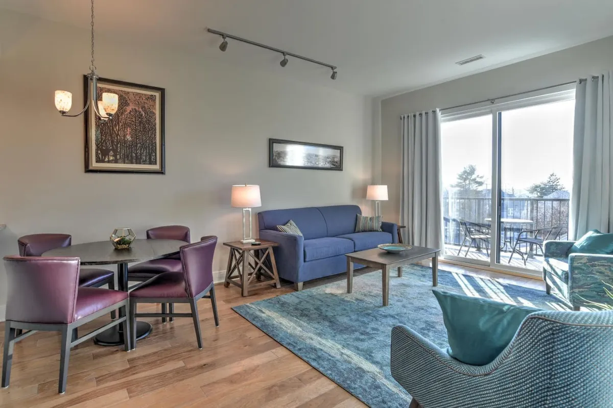 This photo showcases a spacious interior with a blue sofa, dining table, large windows bringing in sunlight, and tasteful decorative artwork. The setup hints at both lively gatherings and tranquil moments, while the expansive windows highlight the airy, urban feel.